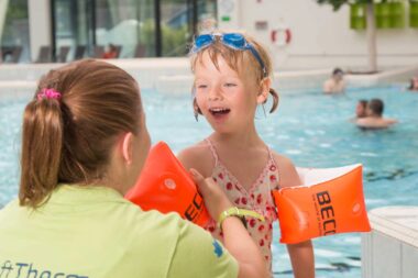 Eine Mitarbeiterin der GraftTherme zieht einem Kleinkind Schwimmflügel an.